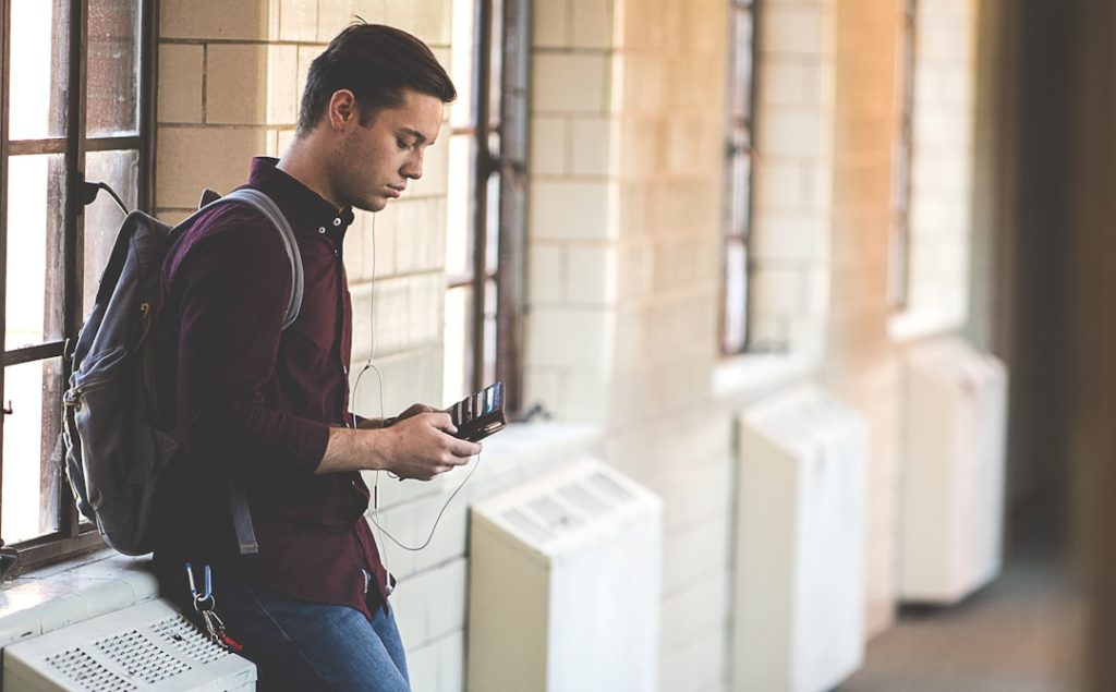Student with backpack checking phone in school hallway — SMS is the fastest way to get BISE board results when the internet is unavailable