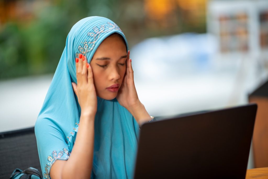 Muslim woman anxiously checking exam results on laptop — represents the stress of waiting for BISE board result online