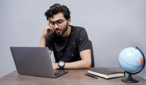 South Asian student checking BISE board results on laptop with books and globe on desk — Photo by fotos.pk on Unsplash