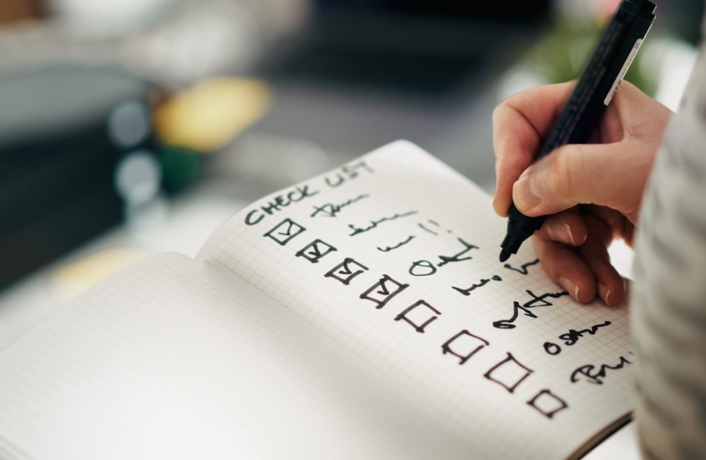 Hand writing a checklist in a notebook representing reviewing rishta proposal fields